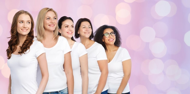 Foto amistad, diversidad, cuerpo positivo y concepto de personas - grupo de mujeres felices de diferentes tamaños en camisetas blancas sobre cuarzo rosa y fondo de luces de serenidad