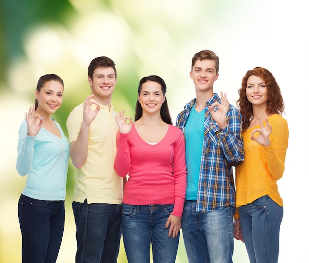 Foto amistad, ecología, gesto y concepto de la gente - grupo de adolescentes sonrientes que muestran el signo de ok sobre el fondo verde