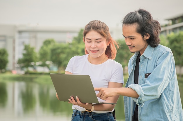 Amistad de gente asiática usando tecnología de computadora portátil al aire libre