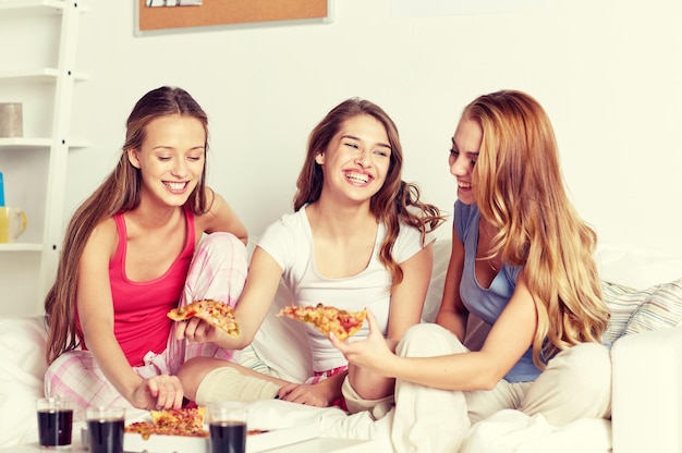 amistad, gente, fiesta de pijamas y concepto de comida chatarra - amigos felices o adolescentes comiendo pizza en casa