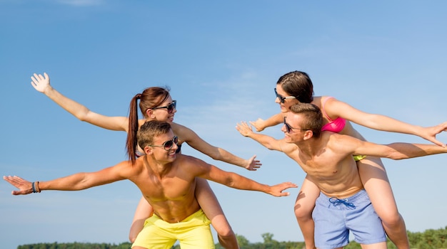 amistad, mar, vacaciones de verano, vacaciones y concepto de la gente - grupo de amigos sonrientes usando trajes de baño y gafas de sol divirtiéndose en la playa