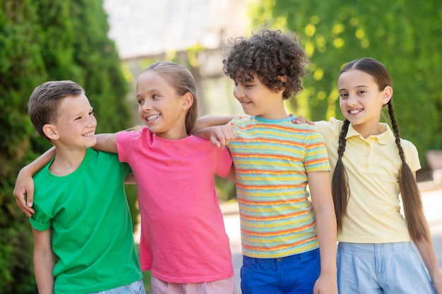 Foto amistad. niños y niñas sonrientes en ropa casual brillante de pie abrazándose en el parque verde el día de verano