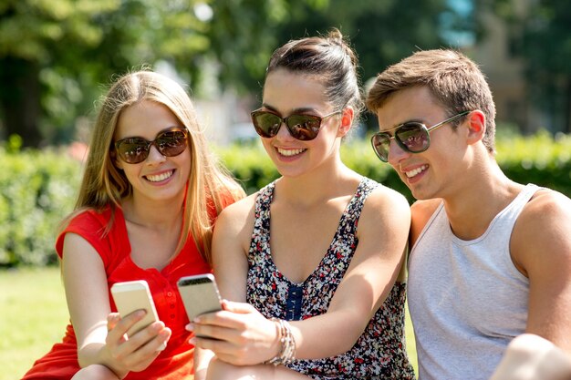 amistad, ocio, verano, tecnología y concepto de personas - grupo de amigos sonrientes con smartphone sentados en el césped en el parque