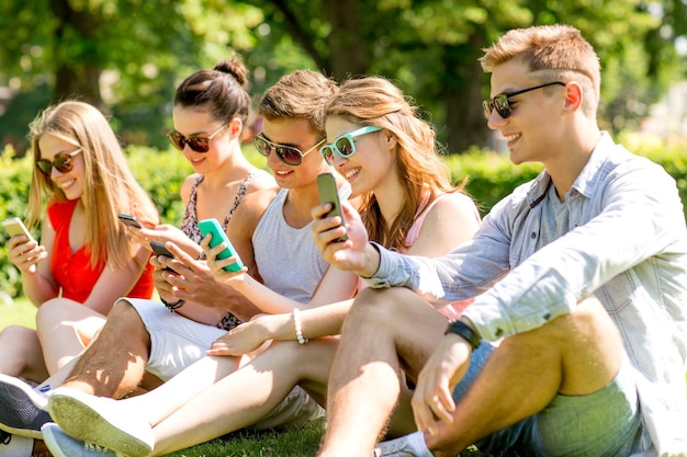 amistad, ocio, verano, tecnología y concepto de personas - grupo de amigos sonrientes con smartphones sentados en el césped en el parque