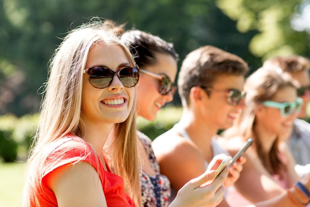 amistad, ocio, verano, tecnología y concepto de personas - grupo de amigos sonrientes con smartphones sentados en el parque