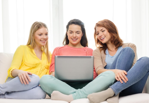 amistad, tecnología y concepto de internet - tres adolescentes sonrientes con computadora portátil en casa