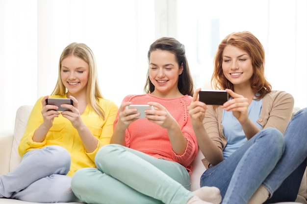 amistad, tecnología y concepto de internet - tres adolescentes sonrientes con smartphones en casa