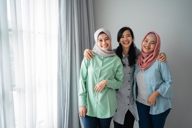 Amistad de tres mujeres sonrientes de pie junto a una ventana