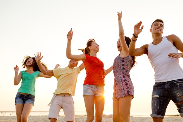 amistad, vacaciones de verano, vacaciones, fiesta y concepto de la gente - grupo de amigos sonrientes bailando en la playa