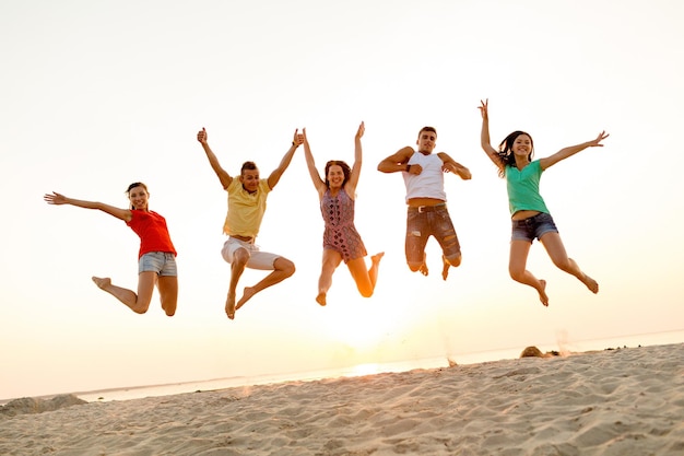 amistad, vacaciones de verano, vacaciones, fiesta y concepto de la gente - grupo de amigos sonrientes bailando y saltando en la playa