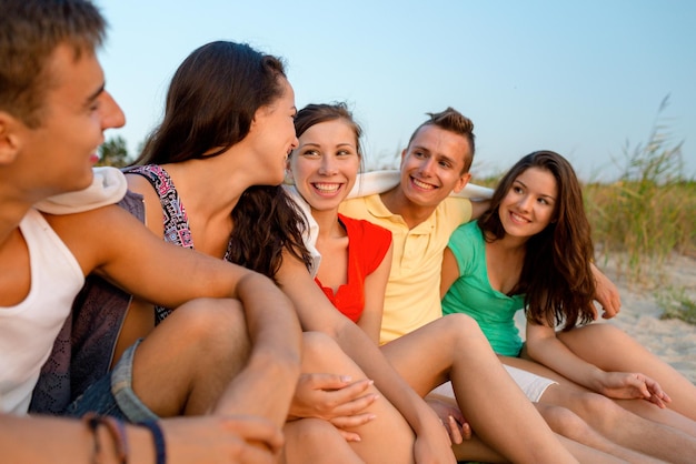 amistad, vacaciones de verano, vacaciones, gesto y concepto de personas - grupo de amigos sonrientes sentados en la playa
