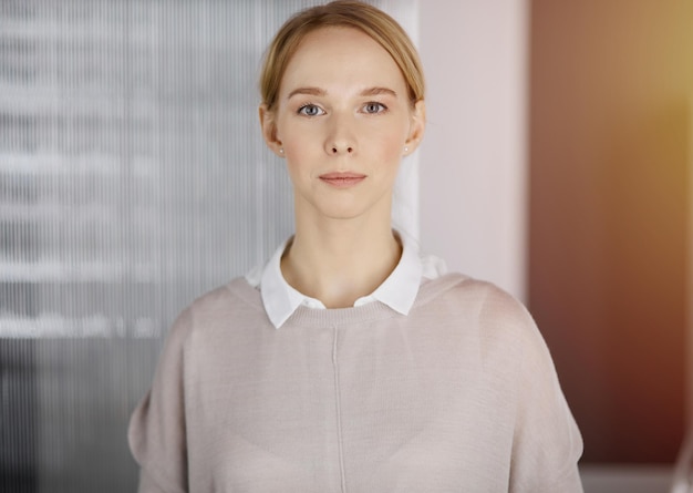 Amistosa mujer de negocios vestida de forma casual para adultos de pie en una oficina soleada. Foto de negocios en la cabeza.