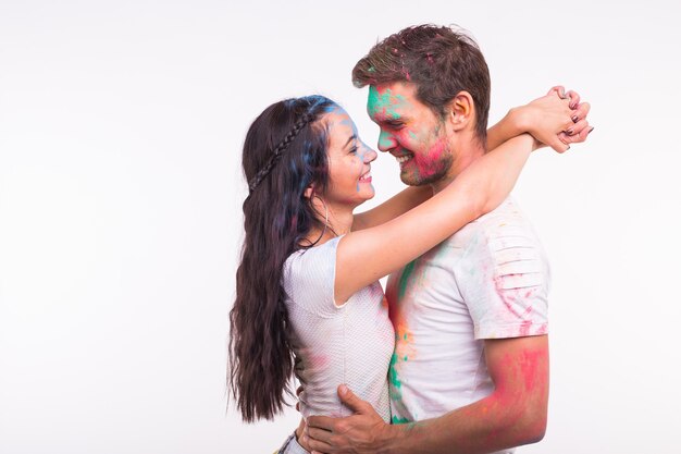 Amizade, amor, festival de holi, conceito de pessoas - jovem casal brincando com cores no festival de holi na superfície branca