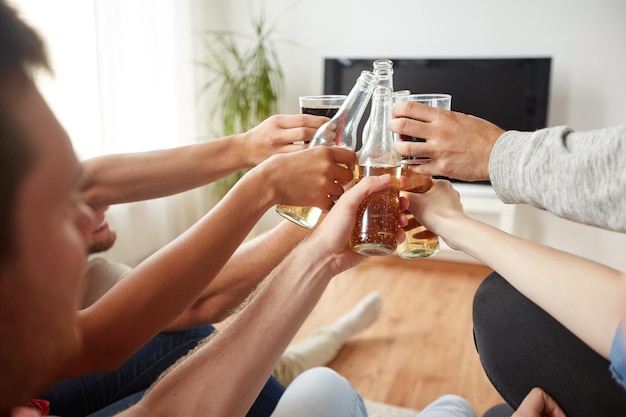 amizade, bebida, álcool, feriados e pessoas conceito - amigos felizes tocando garrafas de cerveja e assistindo televisão em casa