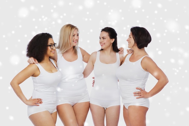 Foto amizade, beleza, corpo positivo e conceito de pessoas - grupo de mulheres felizes diferentes em roupa interior branca sobre a neve