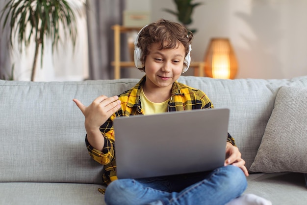 Amizade distante Garotinho falante desfrutando de comunicação online com amigo falando via laptop e fones de ouvido