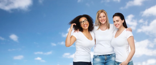 amizade, diversidade, corpo positivo e conceito de pessoas - grupo de mulheres felizes de tamanhos diferentes em camisetas brancas abraçando o céu azul e o fundo das nuvens