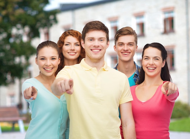 amizade, educação, férias de verão e conceito de pessoas - grupo de adolescentes sorridentes apontando o dedo em você sobre o fundo do campus