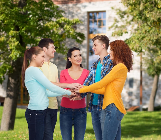 amizade, educação, trabalho em equipe, gesto e conceito de pessoas - grupo de adolescentes sorridentes, colocando a mão uns sobre os outros sobre o fundo do campus