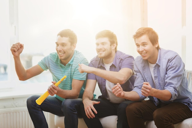 amizade, esportes e entretenimento - amigos do sexo masculino felizes com vuvuzela assistindo esportes em casa