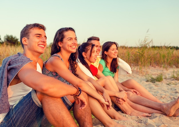 amizade, felicidade, férias de verão, feriados e conceito de pessoas - grupo de amigos sorridentes sentados na praia