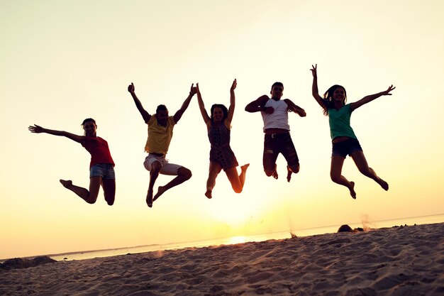 amizade, férias de verão, feriados, festa e conceito de pessoas - grupo de amigos sorridentes dançando e pulando na praia