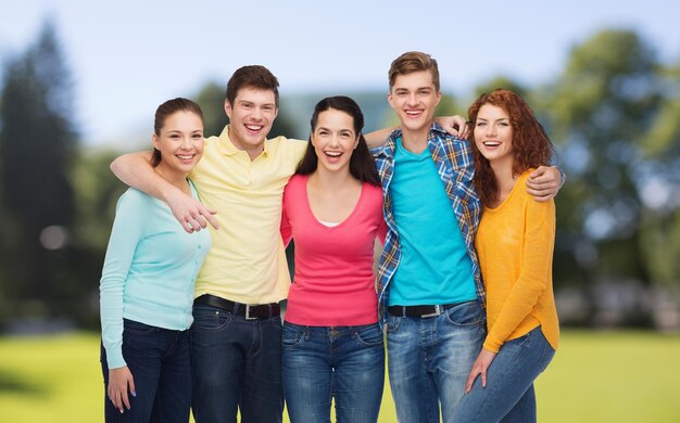 amizade, férias de verão, natureza e conceito de pessoas - grupo de adolescentes sorridentes em pé e abraçando sobre o fundo do parque verde