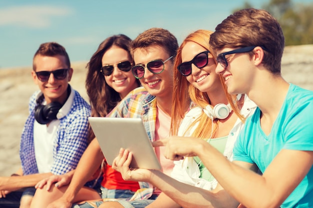 amizade, lazer, verão e conceito de pessoas - grupo de amigos sorridentes com computador tablet pc sentado ao ar livre