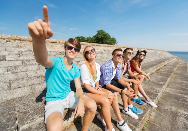 amizade, lazer, verão, gesto e conceito de pessoas - grupo de amigos sorridentes sentados e apontando o dedo na rua da cidade