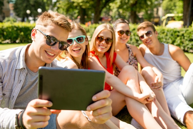 Amizade, lazer, verão, tecnologia e conceito de pessoas - grupo de amigos sorridentes com computador tablet pc fazendo selfie no parque
