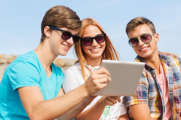 amizade, lazer, verão, tecnologia e conceito de pessoas - grupo de amigos sorridentes com computador tablet pc sentado ao ar livre