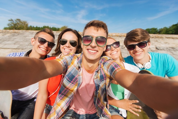 amizade, lazer, verão, tecnologia e conceito de pessoas - grupo de amigos sorridentes com skate fazendo selfie ao ar livre