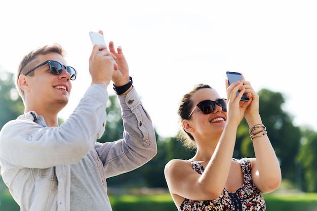 amizade, lazer, verão, tecnologia e conceito de pessoas - grupo de amigos sorridentes com smartphone tirando foto ao ar livre