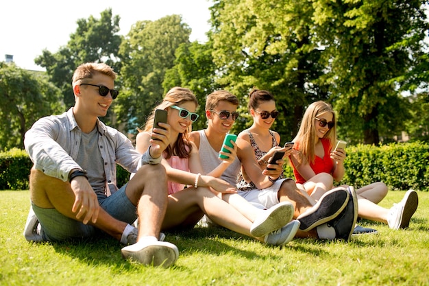 amizade, lazer, verão, tecnologia e conceito de pessoas - grupo de amigos sorridentes com smartphones sentados na grama no parque