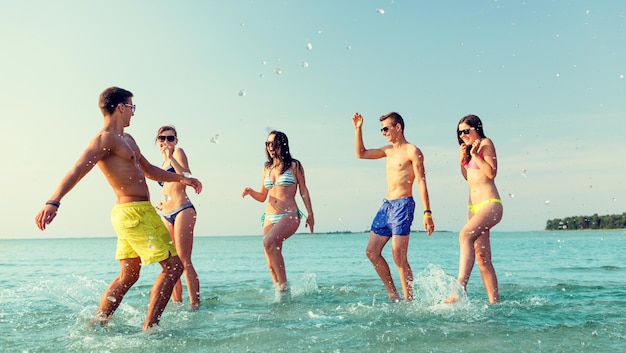amizade, mar, férias de verão, feriados e conceito de pessoas - grupo de amigos felizes se divertindo na praia
