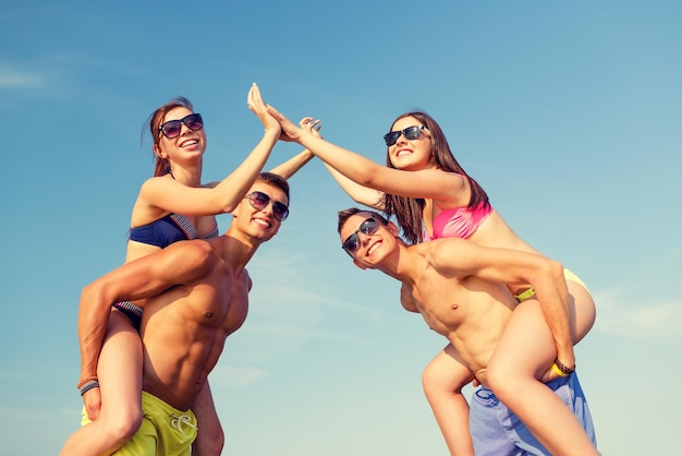 amizade, mar, gesto, férias e conceito de pessoas - grupo de amigos sorridentes vestindo trajes de banho se divertindo e fazendo mais cinco na praia