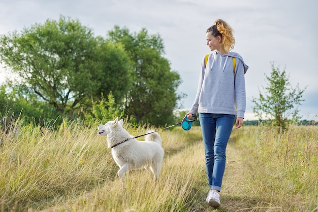 Amizade meninas e cachorros, adolescente e cachorro husky caminhando ao ar livre, bela paisagem natureza prado céu nublado