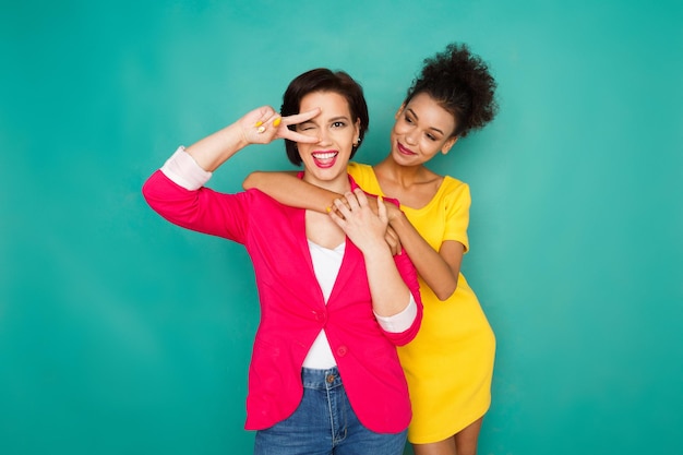 Amizade multiétnica e conceito de suporte. Garotas mulatas e caucasianas em roupas casuais coloridas se abraçando e se divertindo no fundo azul do estúdio com espaço de cópia