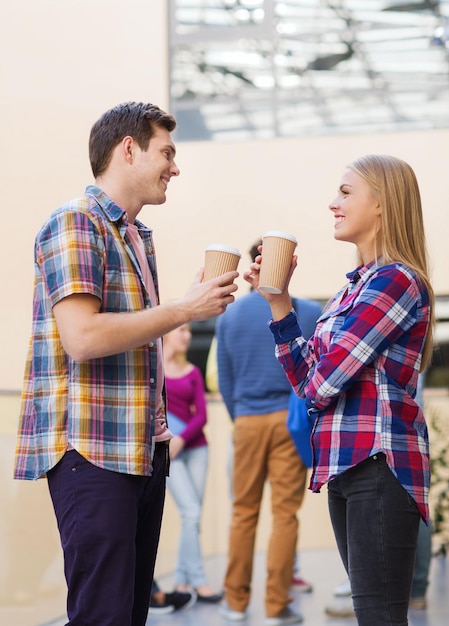 amizade, pessoas, bebidas e conceito de educação - grupo de estudantes sorridentes com xícaras de café de papel ao ar livre