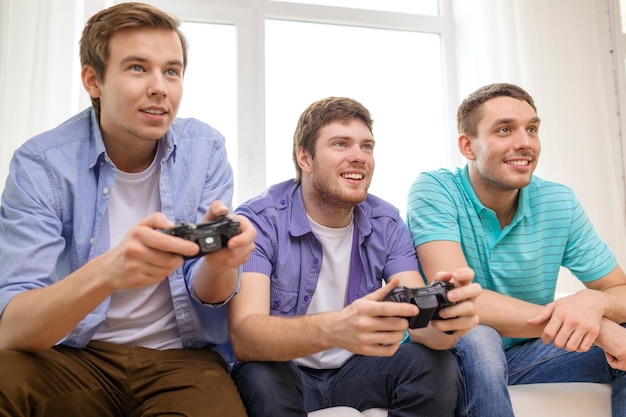 amizade, tecnologia, jogos e conceito de casa - amigos do sexo masculino sorridentes jogando videogame em casa