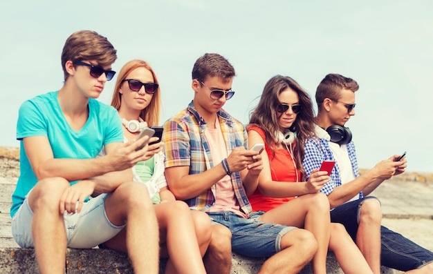 amizade, verão, tecnologia e conceito de pessoas - grupo de amigos com smartphones e fones de ouvido ao ar livre