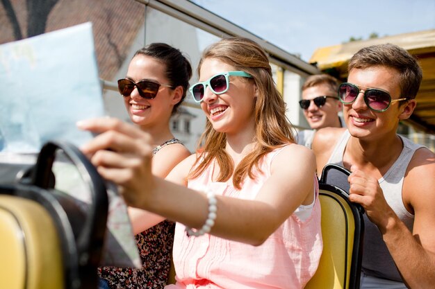 Amizade, viagens, férias, verão e conceito de pessoas - grupo de amigos sorridentes com mapa viajando de ônibus de turismo