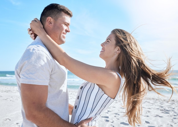 Amo a praia e o verão com um casal se abraçando na areia à beira-mar ou oceano durante as férias juntos Sorriso feliz e romance com um homem e uma mulher se unindo durante as férias ou quebrando na água