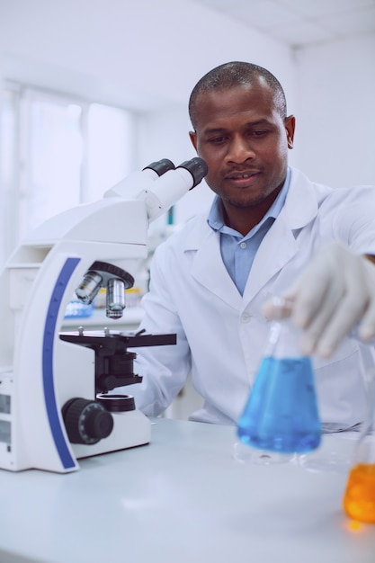 Amo bioengenharia. biólogo inteligente e experiente trabalhando com seu microscópio e segurando um tubo