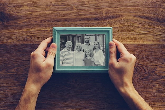 Foto ¡amo a mi familia! vista superior de primer plano del hombre sujetando la fotografía de su familia sobre un escritorio de madera