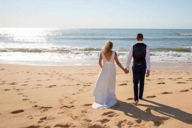 Amo a la novia y al novio caminando en la playa de arena del océano en el día de la boda