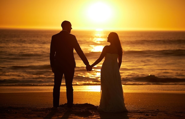 Amo o verão e o casal em uma praia ao pôr do sol silhueta de mãos dadas e ligação com vistas para o mar na natureza Viagens românticas e natureza com homem e mulher desfrutando de lua de mel no mar e viagem romântica