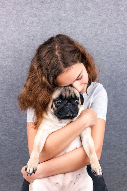 Amor animal de estimação. Menina adolescente encaracolado abraça seu cachorro pug triste com amor