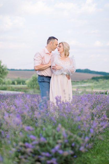 Amor, aniversario de bodas de plata. Feliz pareja caucásica madura romántica, posando juntos mirando el uno al otro, mientras camina al aire libre en el hermoso campo de lavanda