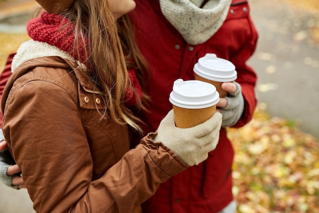 El amor, las bebidas y el concepto de la gente: cerca de una pareja joven feliz con tazas de café en el parque de otoño